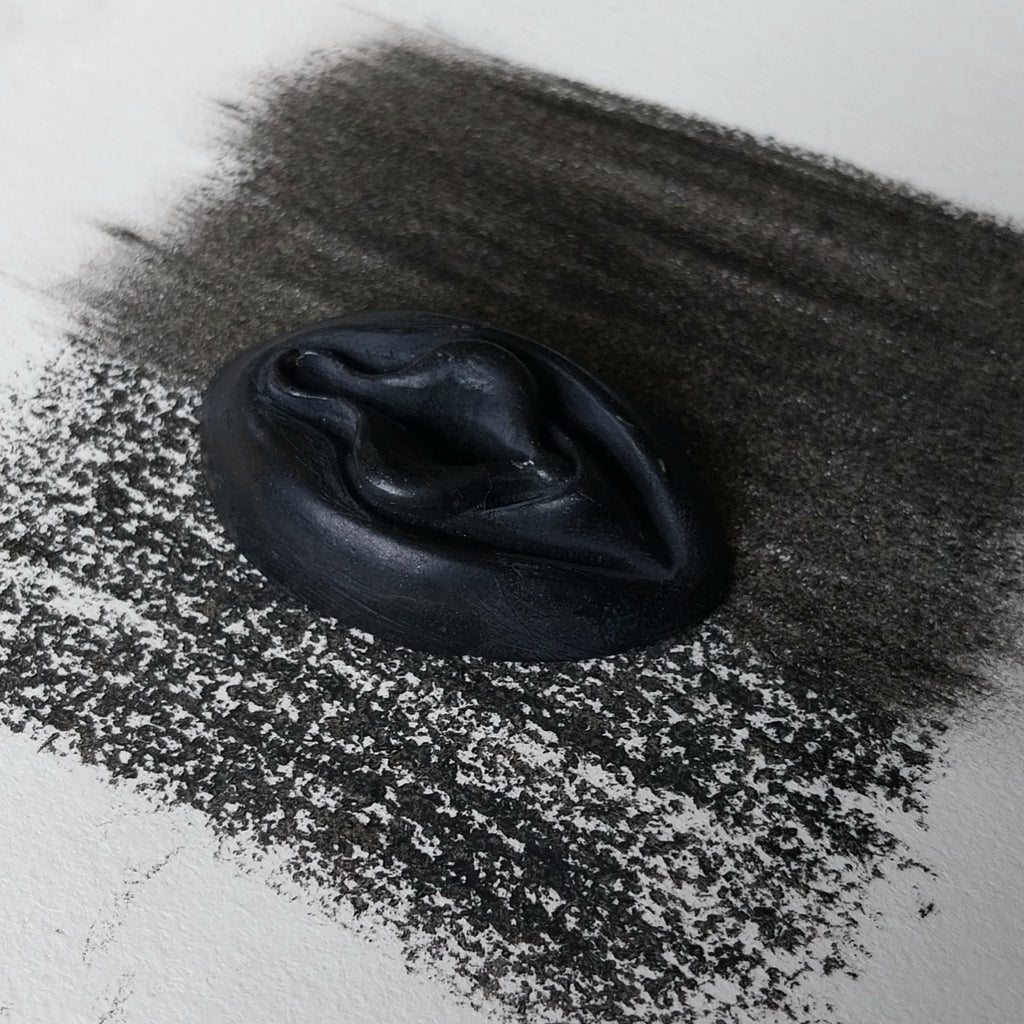 Crayon de subversion VULVA NATURALIS noir, vue de profil. Crayon de cire, pastel gras. Dépose de couleur sur une feuille puis estompe au doigt