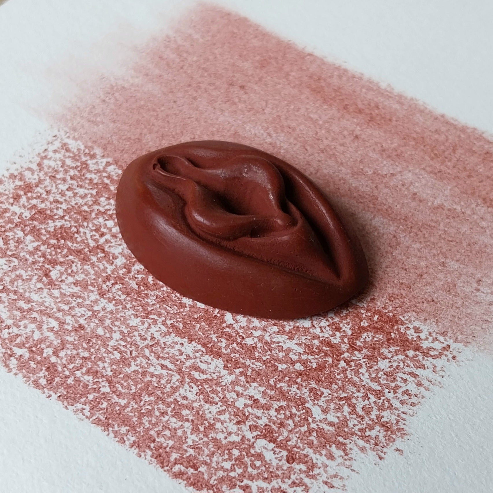 Crayon de subversion VULVA NATURALIS bordeau, vue de profil. Crayon de cire, pastel gras. Dépose de couleur sur une feuille puis estompe au doigt