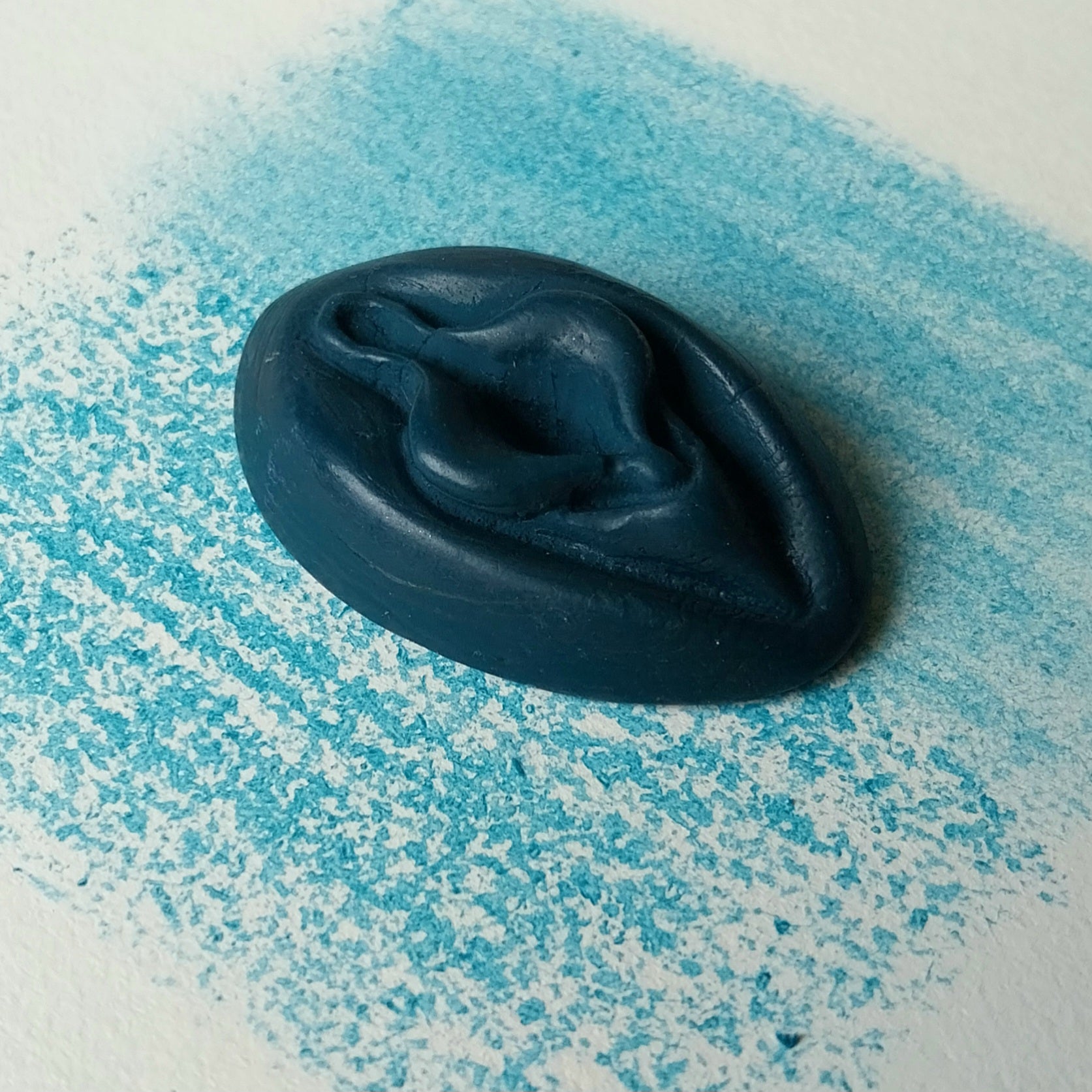 Crayon de subversion VULVA NATURALIS bleu canard, vue de profil. Crayon de cire, pastel gras. Dépose de couleur sur une feuille puis estompe au doigt