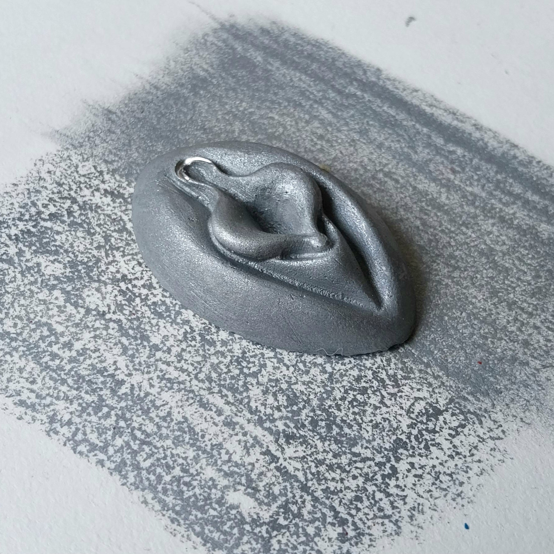 Crayon de subversion VULVA NATURALIS argenté, vue de profil. Crayon de cire, pastel gras. Dépose de couleur sur une feuille puis estompe au doigt
