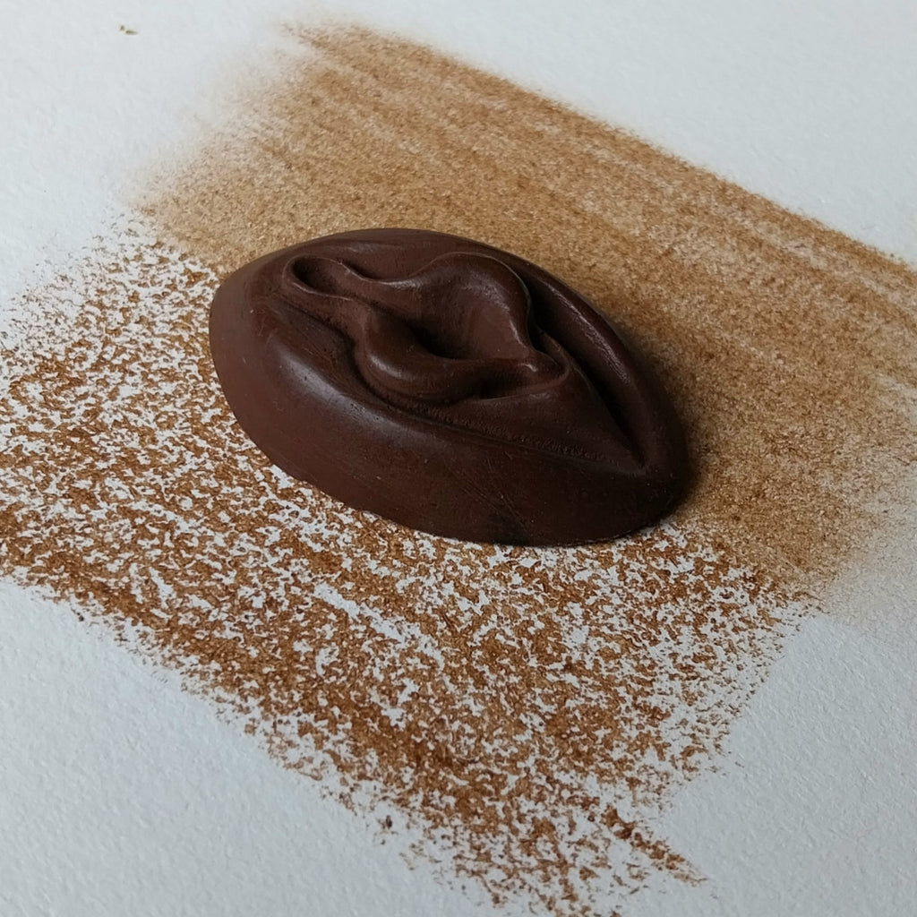 Crayon de subversion VULVA NATURALIS chocolat, vue de profil. Crayon de cire, pastel gras. Dépose de couleur sur une feuille puis estompe au doigt